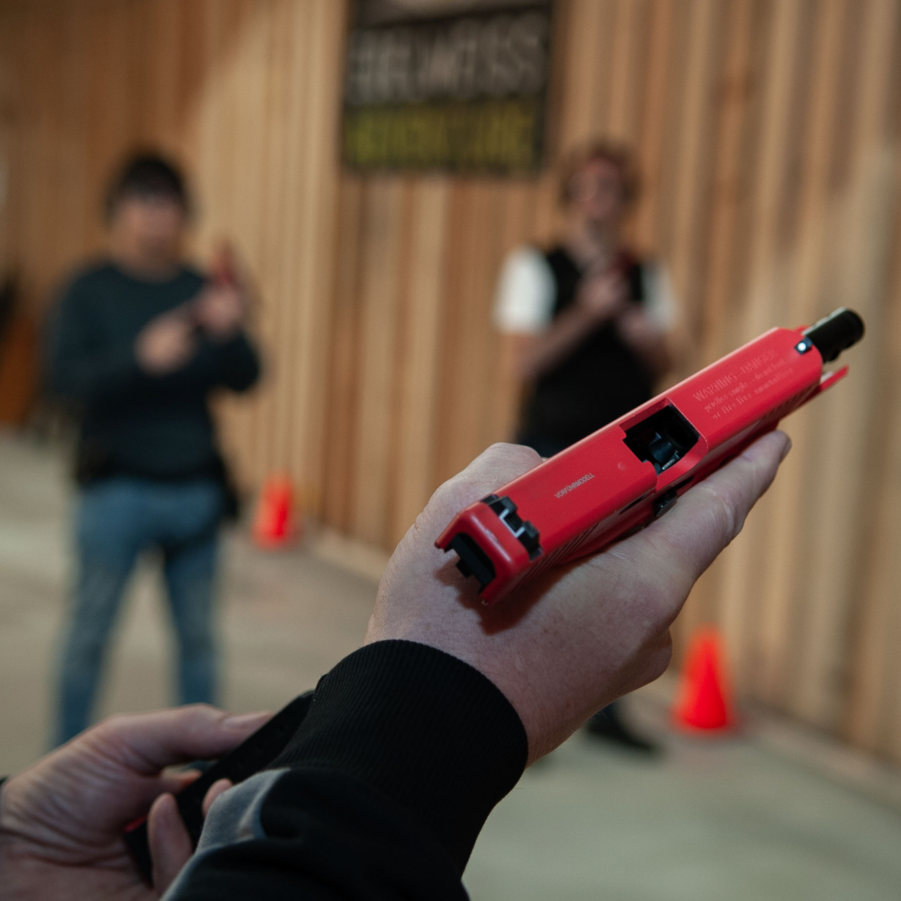 Die Hand des Schießtrainers mit einr Rotwaffe groß im Vordergrund und dahinter zwei angehende Sportschützen die zum ersten Mal mit einer Pistole schießen