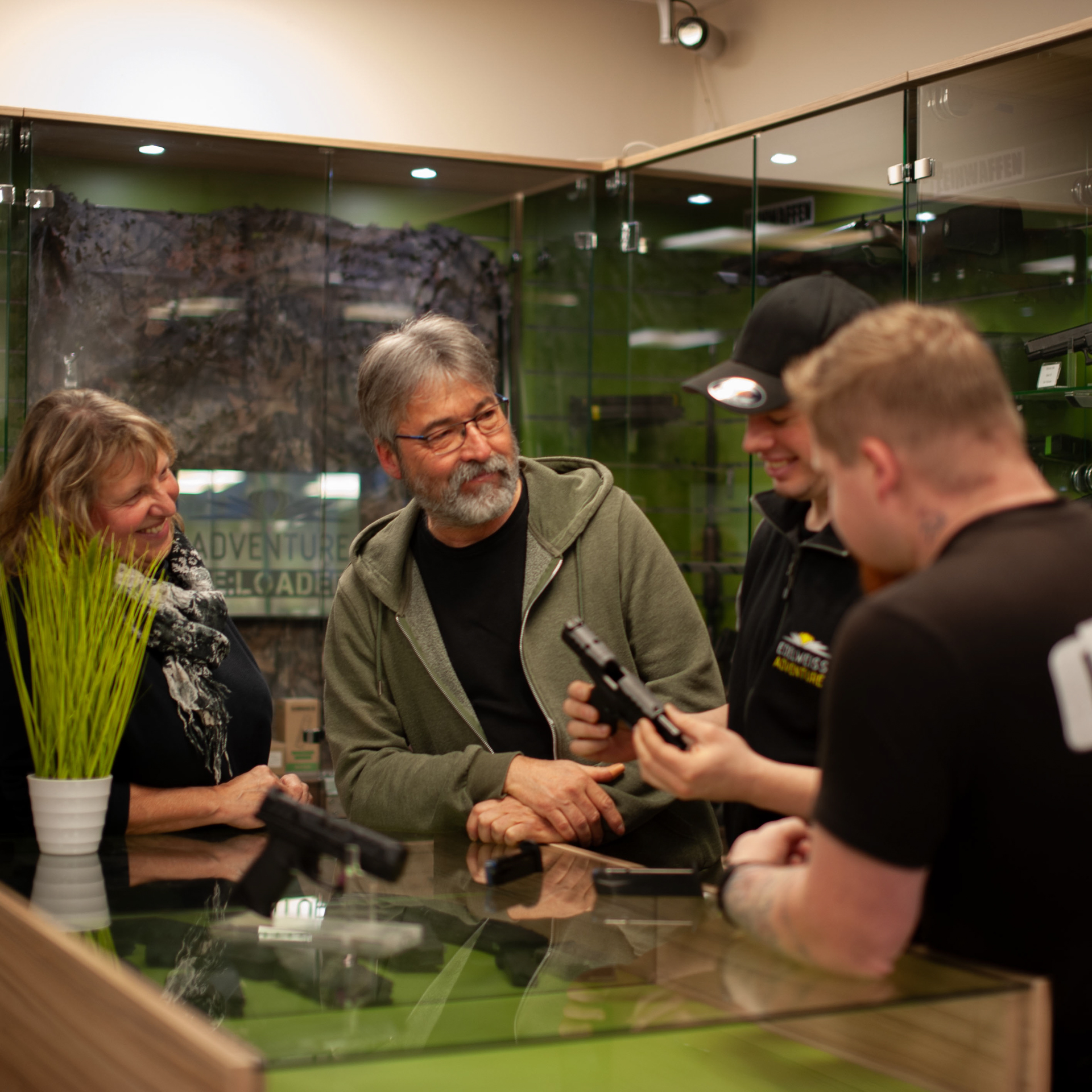 Waffenexperte berät eine Kundin und zwei Kunden über Pistolen